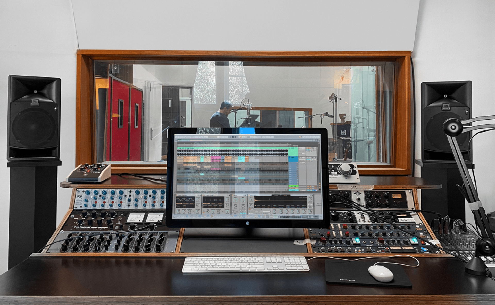 Looking through to a studio recording floor from a control room with outboard audio equipment