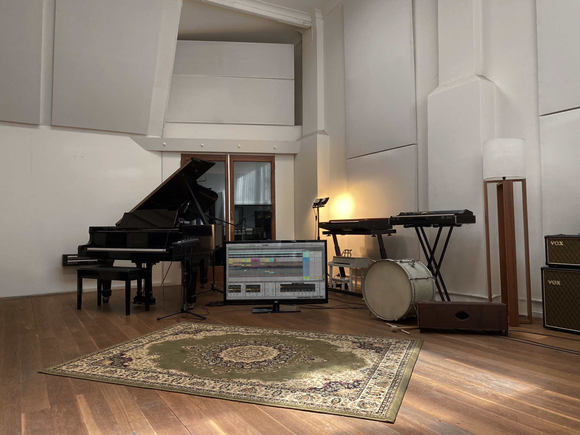 large recording room with persian rug, baby grand piano, bass drum and vintage keyboards